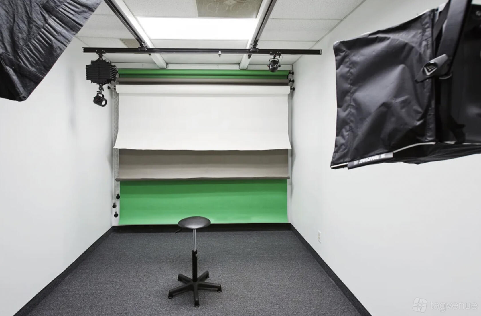 A photo studio with green and white backdrop rolls, softbox lighting, and a single black stool at Jason Kindig Photography.