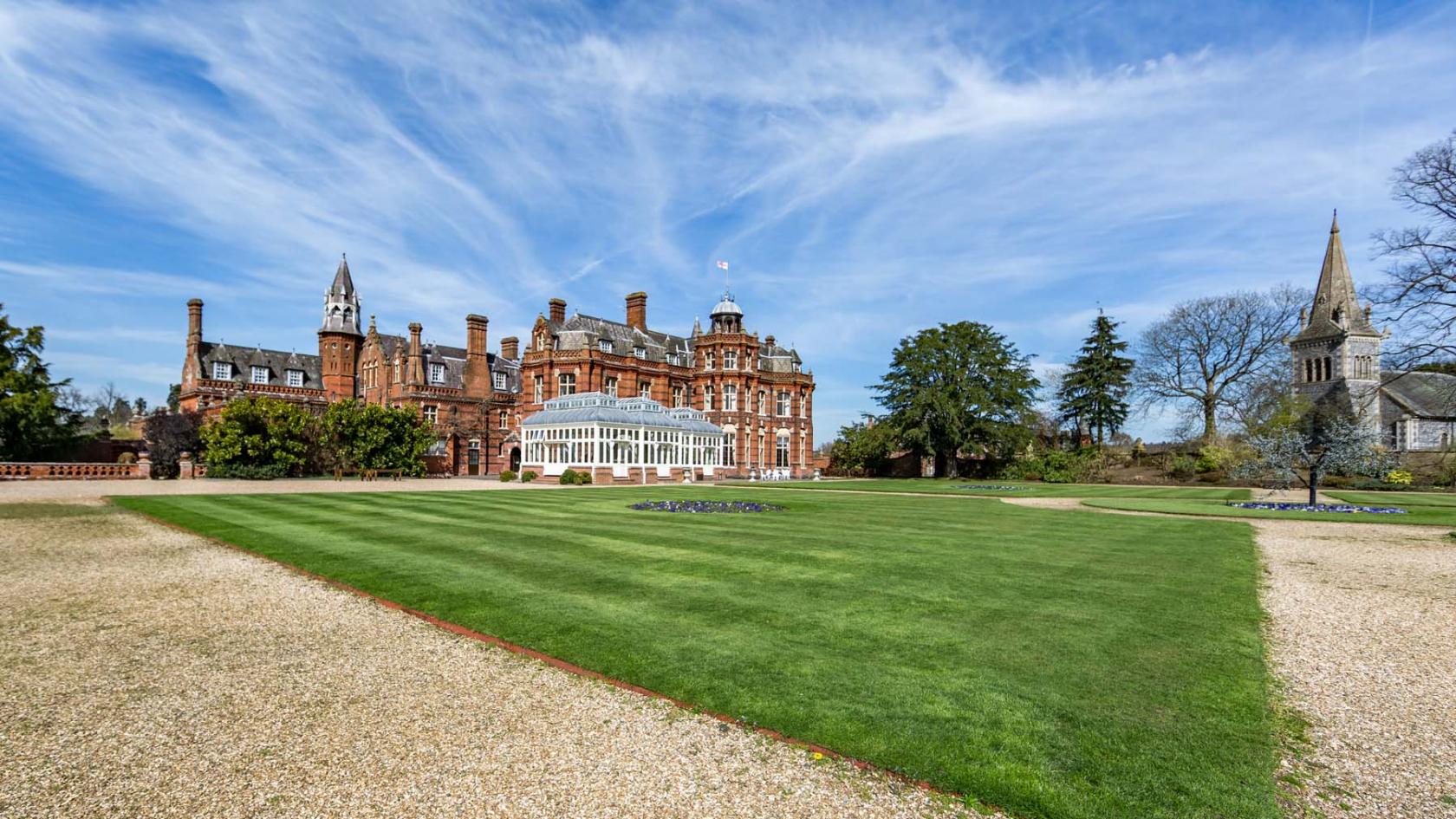 A historic red-brick event venue with a glass conservatory and expansive manicured lawn at The Elvetham Hotel.