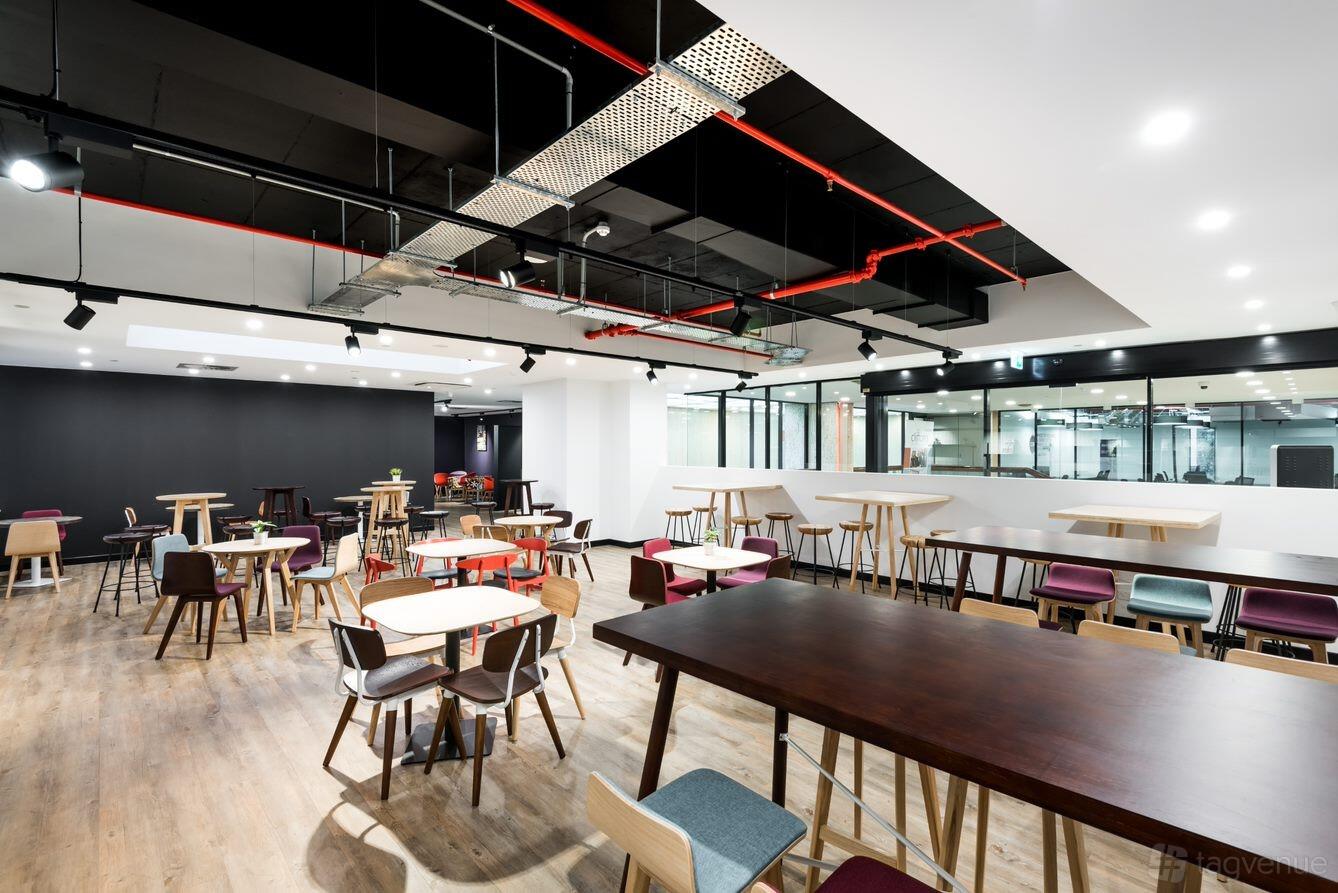An event space with wood flooring, scattered tables and chairs, and exposed ceiling pipes at Cliftons Perth.