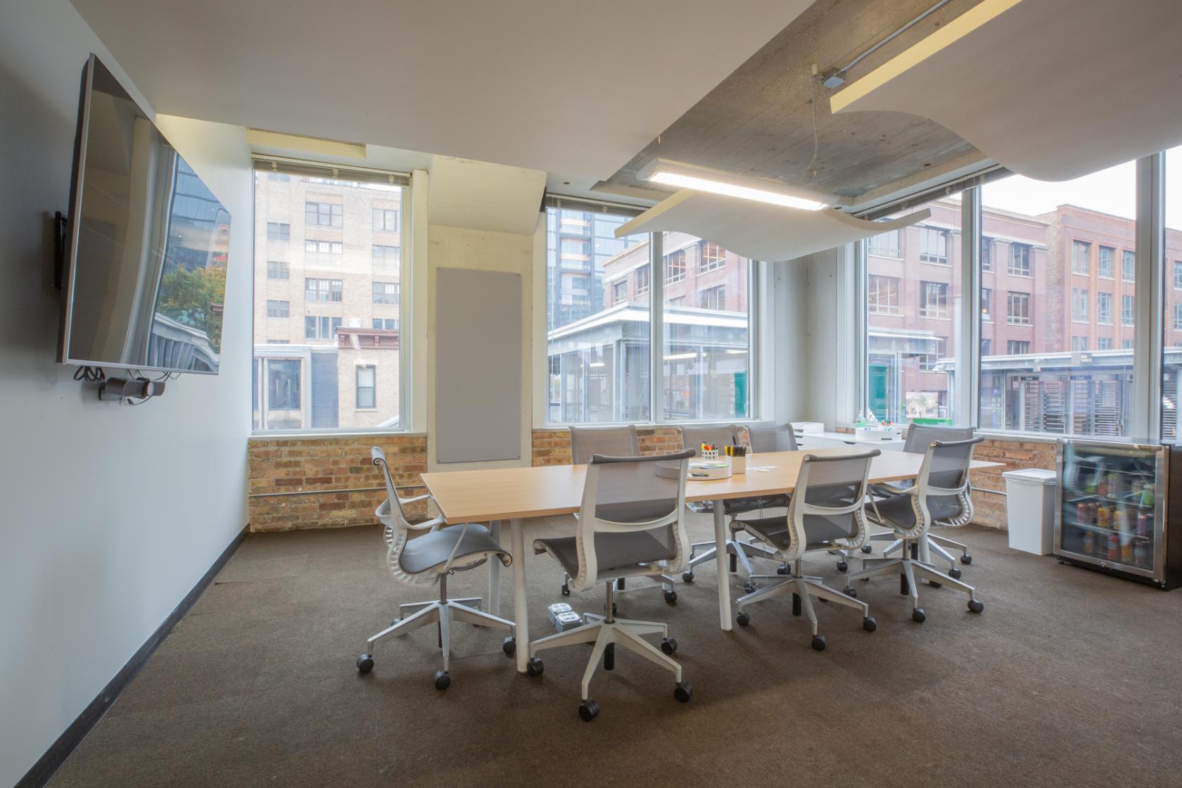 A meeting room with floor-to-ceiling windows, exposed brick walls, and a large screen at One Three Workspace.