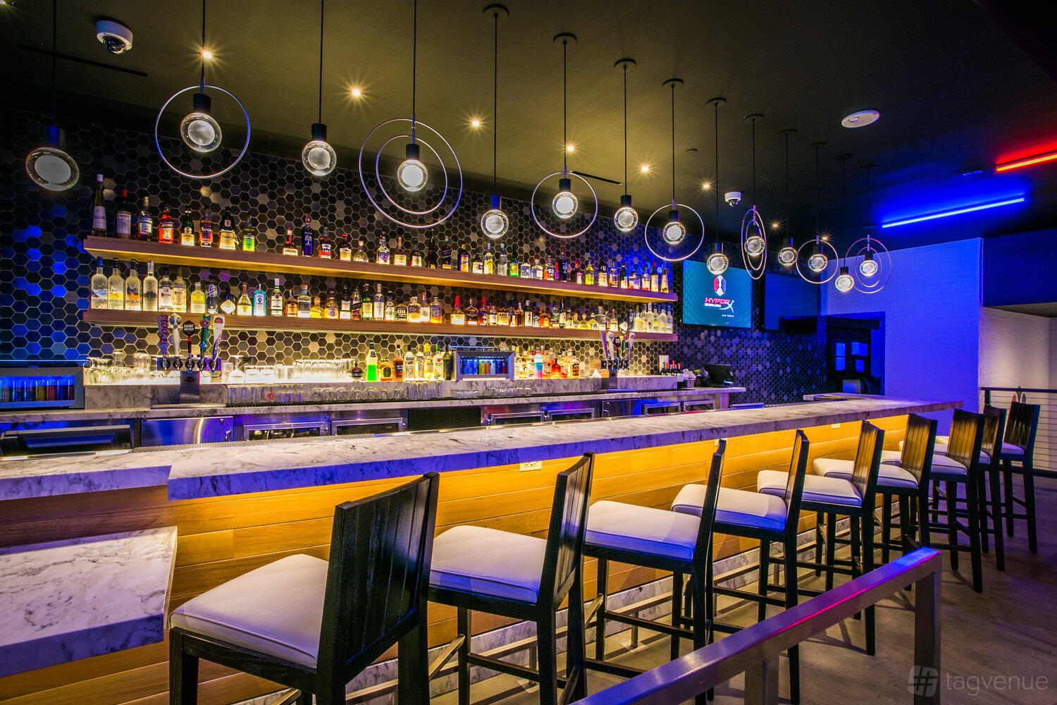 An event space with a marble-topped bar, illuminated shelves stocked with bottles, and modern pendant lights at HyperX Arena Las Vegas.