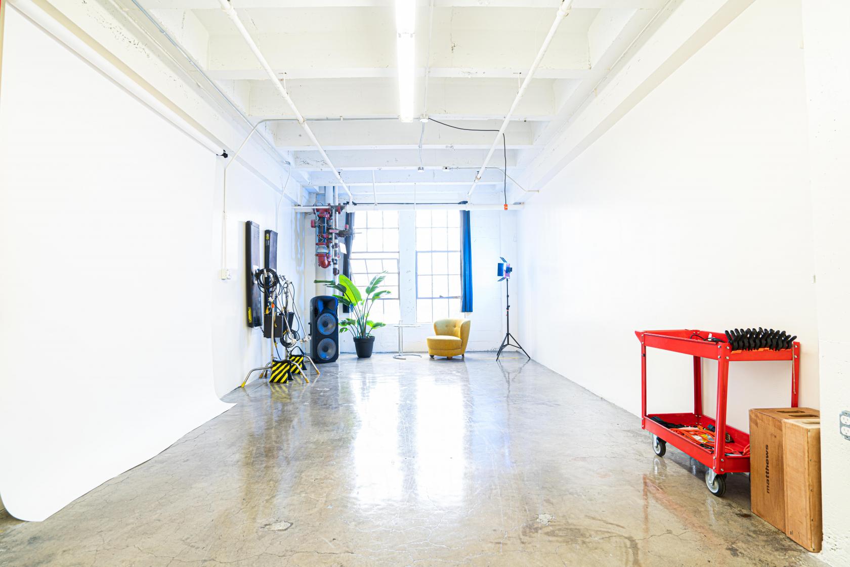 A photo studio with white walls, polished concrete floors, a seamless backdrop, and a yellow armchair at Studio Stupendous.