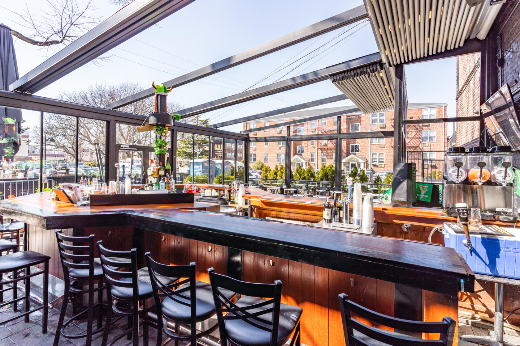 A terrace with a covered bar, rows of black barstools, and glass walls at One Station Plaza.