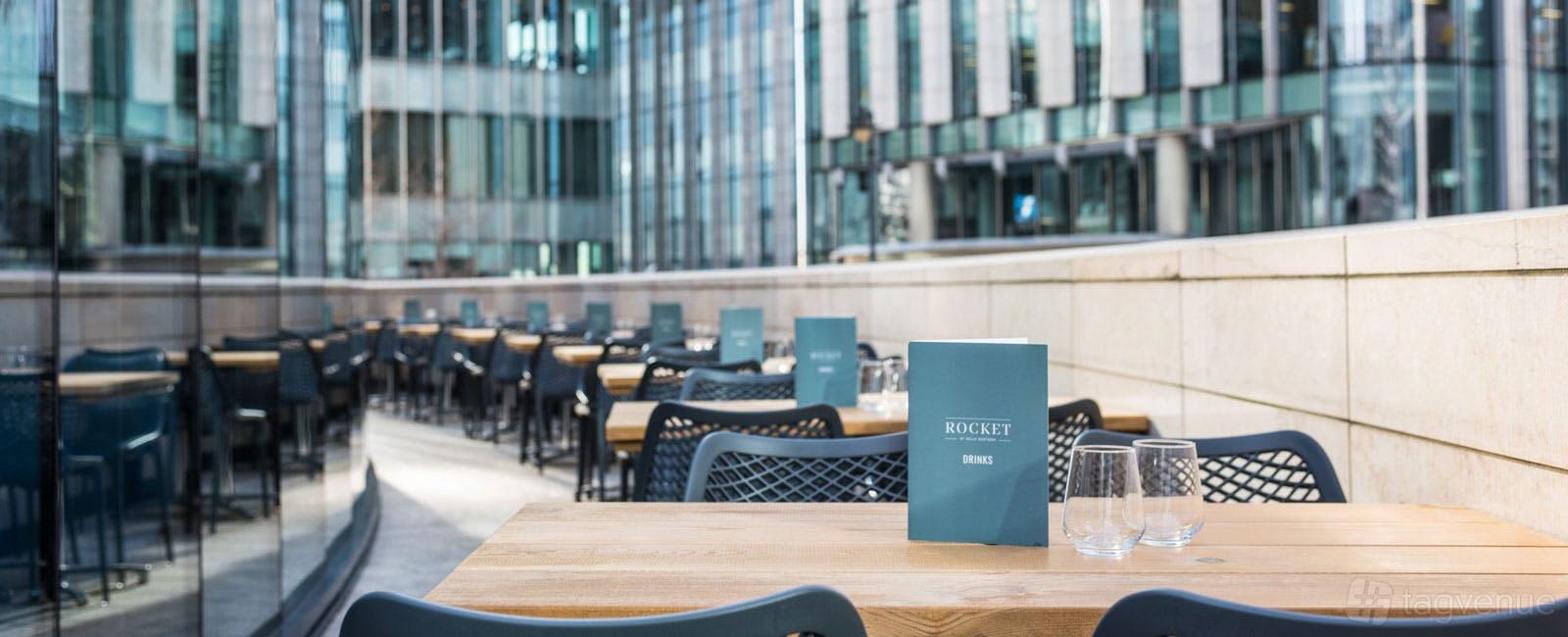 An outdoor restaurant patio with wooden tables, black chairs, and Rocket menus at Rocket