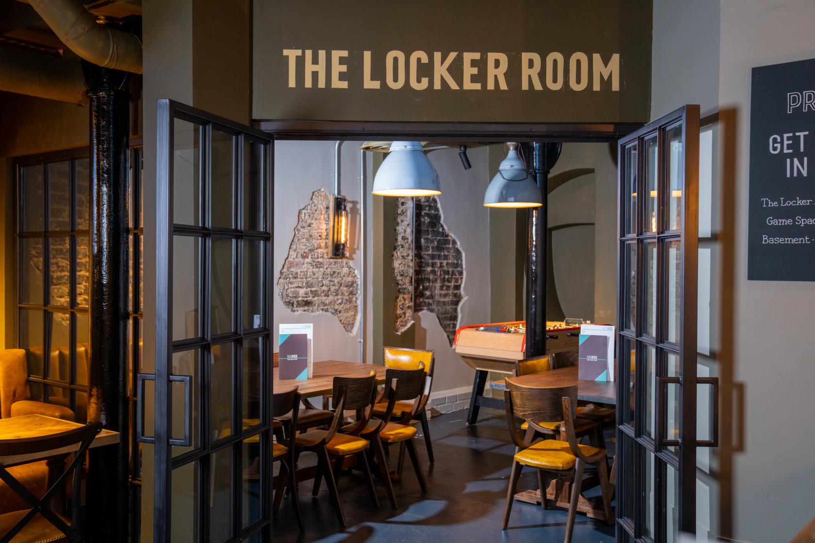 A bar with exposed brick accents, pendant lighting, and wooden tables next to a foosball table at Bar Kick.