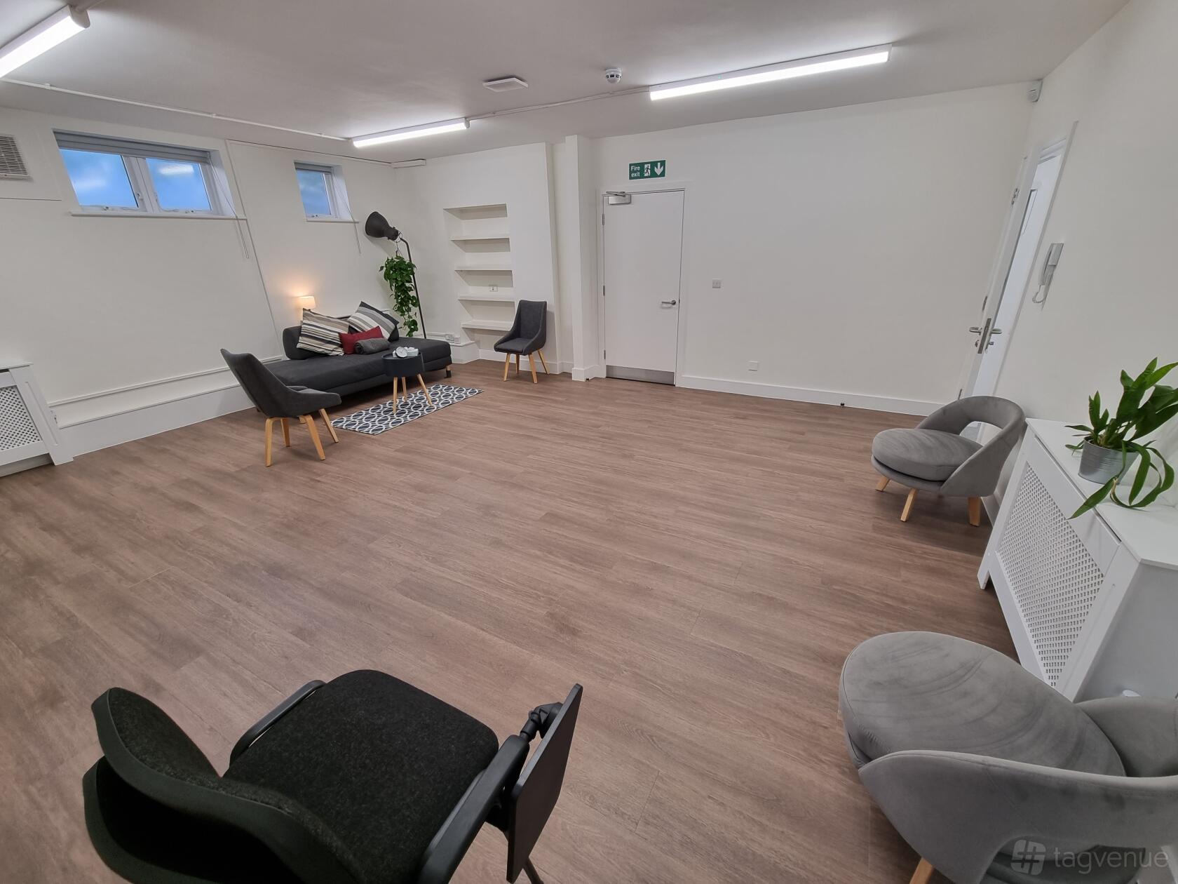 A meeting room with wood flooring, neutral walls, lounge seating, and potted plants at Strides HCC.