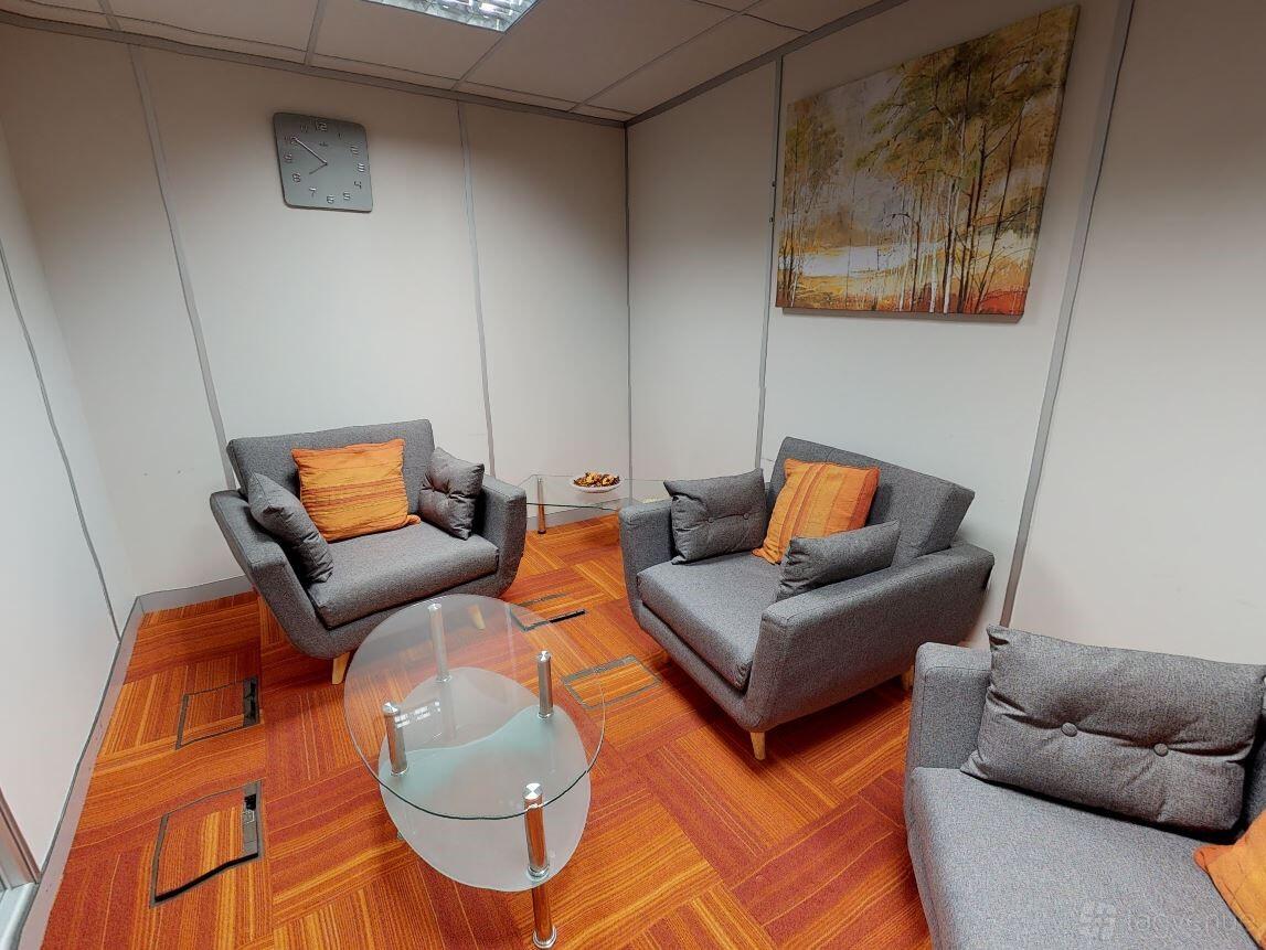 A meeting room with grey armchairs, orange accent pillows, and a glass coffee table at Portal Business Centre Dallam Court.
