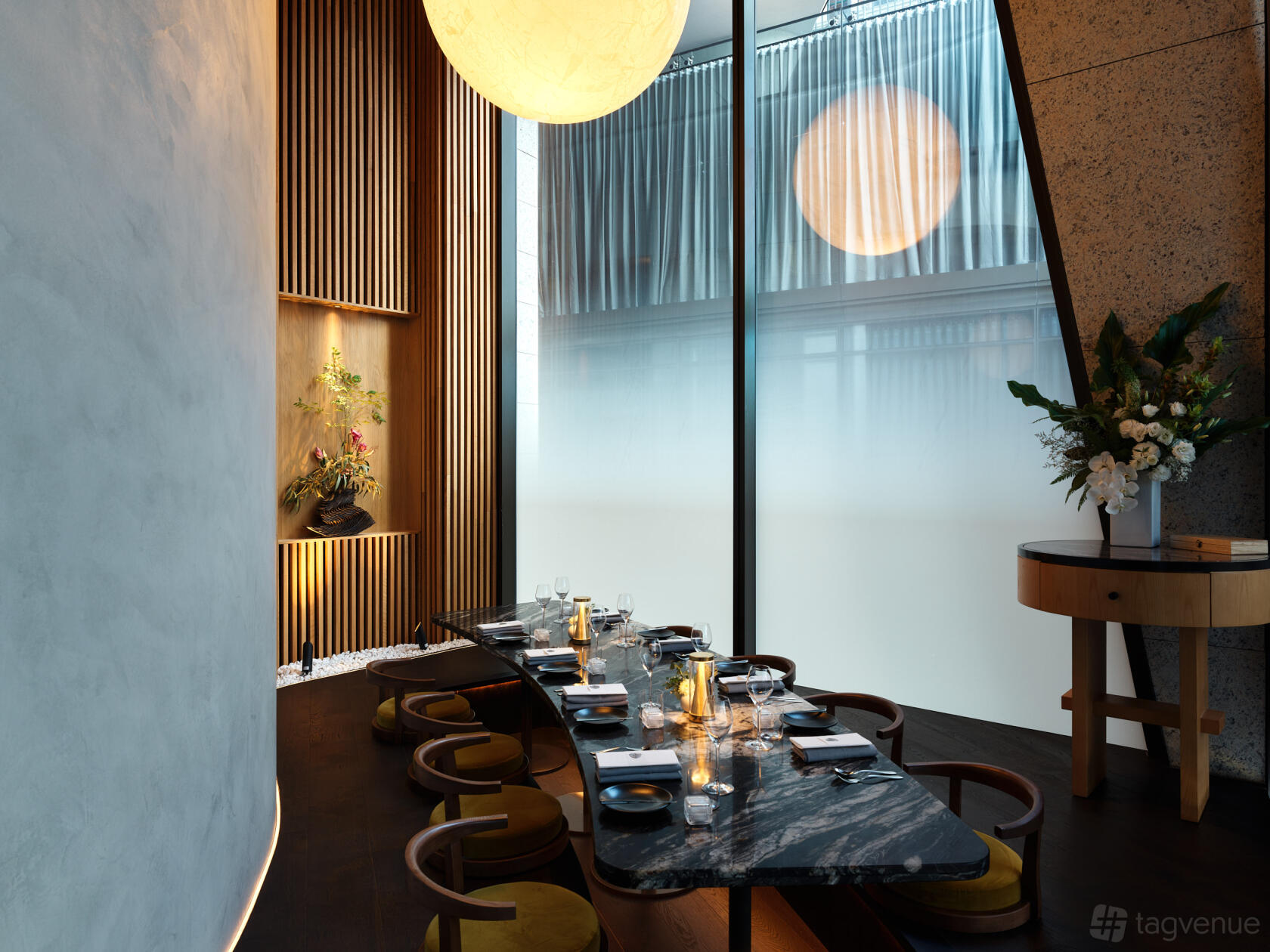 A dining room with a long black table, wood slat wall, large globe pendant light, and floor-to-ceiling windows at Oborozuki.