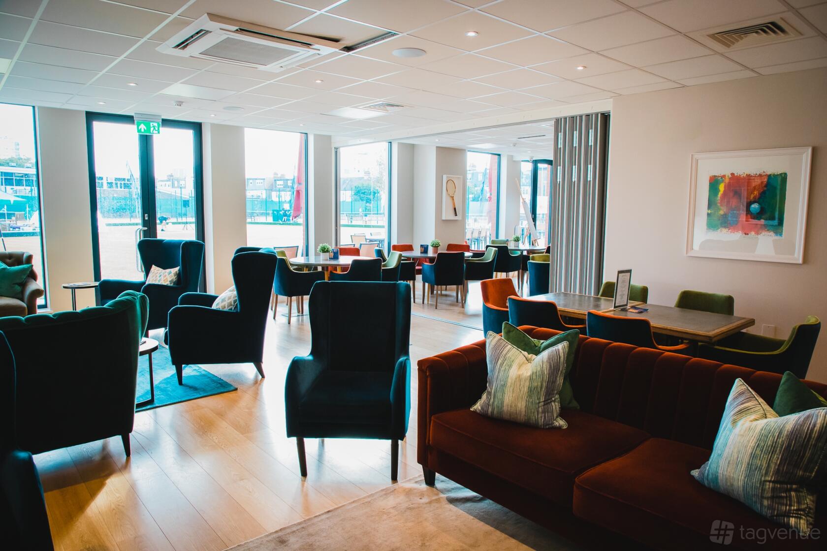 A lounge with velvet armchairs, modern art, and floor-to-ceiling windows at Parsons Green Club.