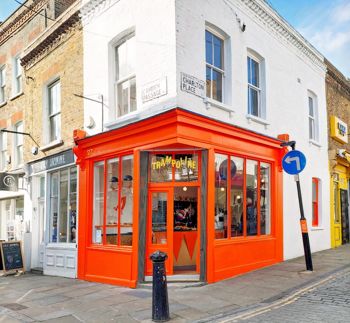 A café with bright orange window frames and signage on a street corner at Trampoline.