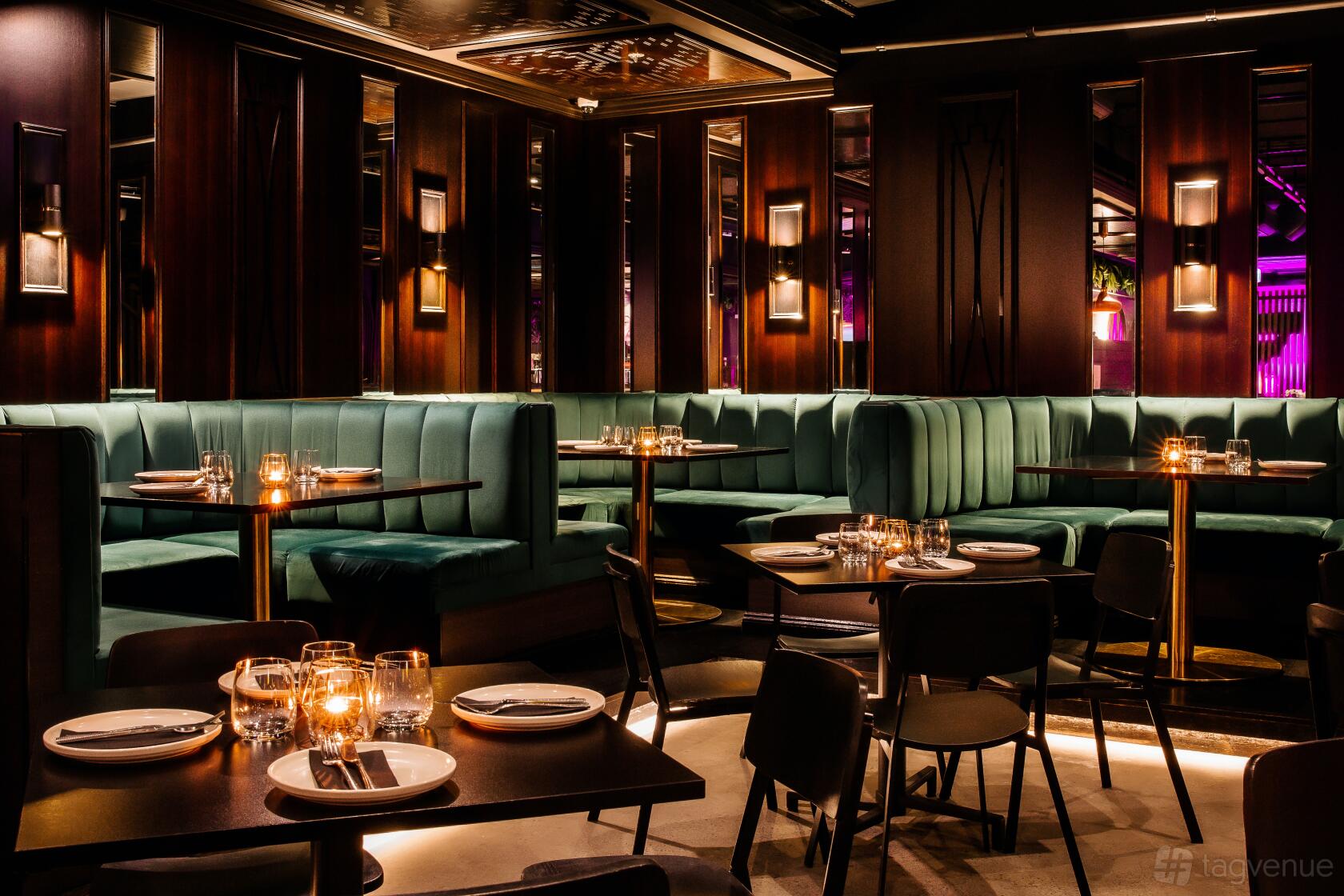 A dining room with teal velvet banquette seating, dark wood paneling, and candlelit tables at Mr. Mista.