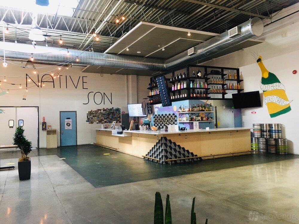 A spacious bar with an industrial ceiling, large mural, and a long counter backed by shelves at Native Son - Inland Empire.