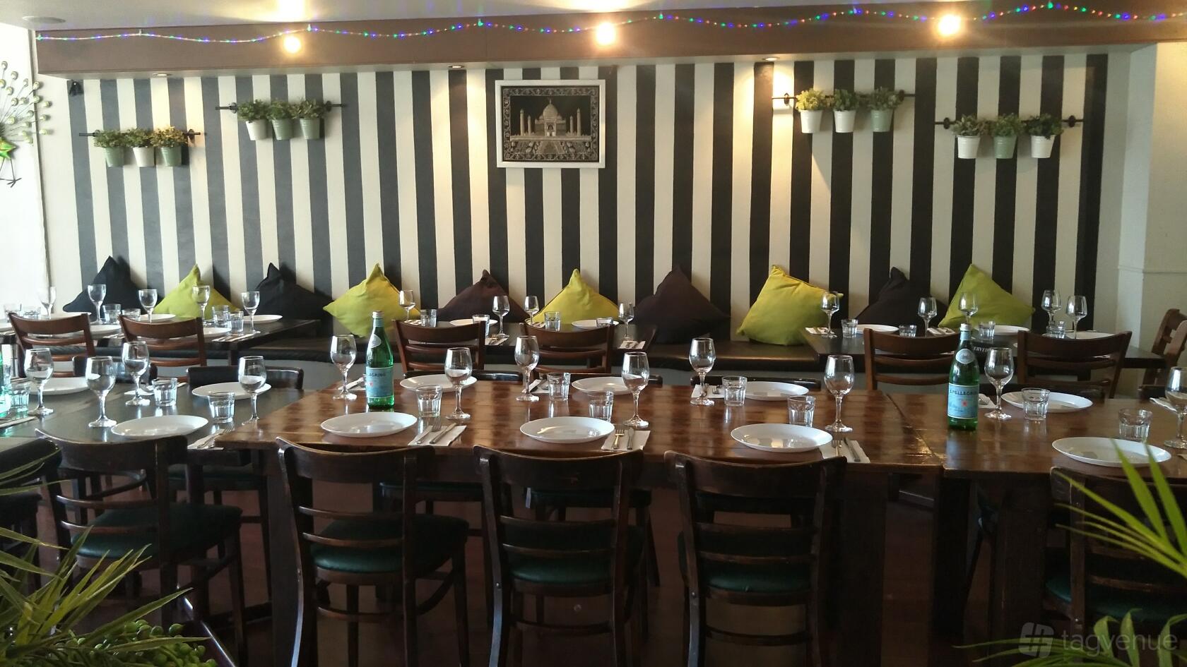 A restaurant with striped walls, bench seating with colorful cushions, and tables set with plates and glassware at Gurtaj Indian Restaurant & Takeaway.