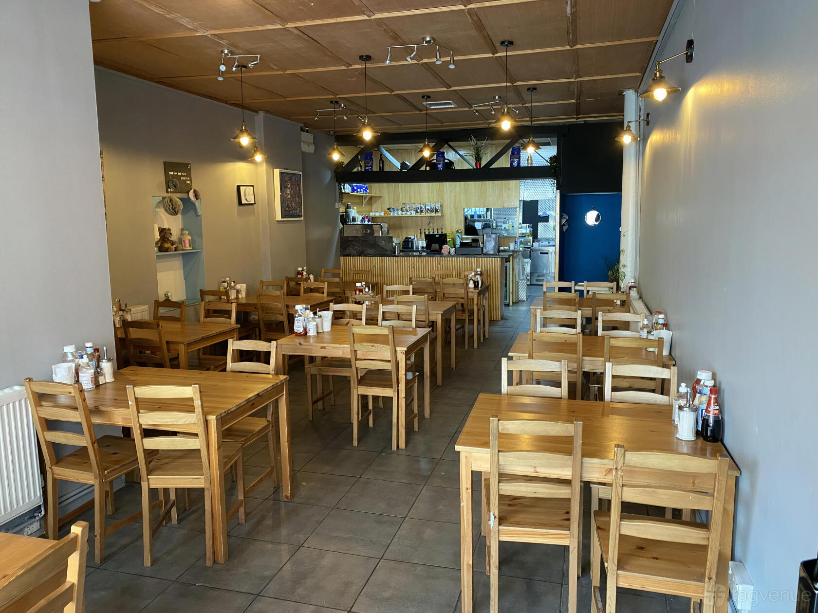 A cafe with wooden tables and chairs, condiment bottles on each table, and tiled flooring at Cafe On The Hill.