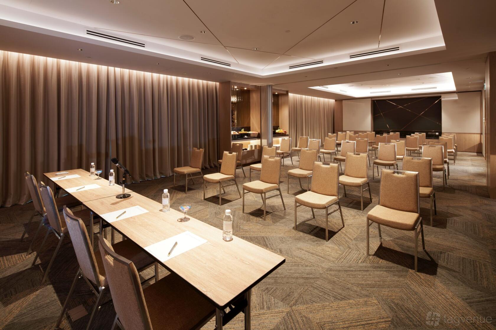 A hotel function room with rows of beige chairs, conference tables, and floor-to-ceiling curtains at Orchard Grand Court.