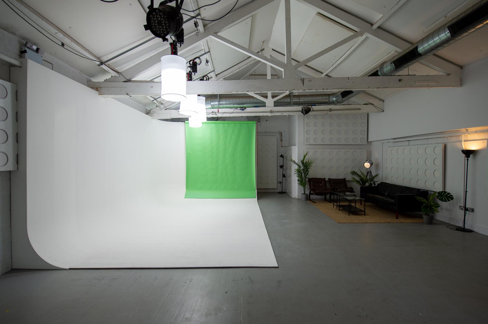 A rehearsal studio with a white cyclorama, green screen backdrop, lighting rigs, and a lounge area at Factory Studios.