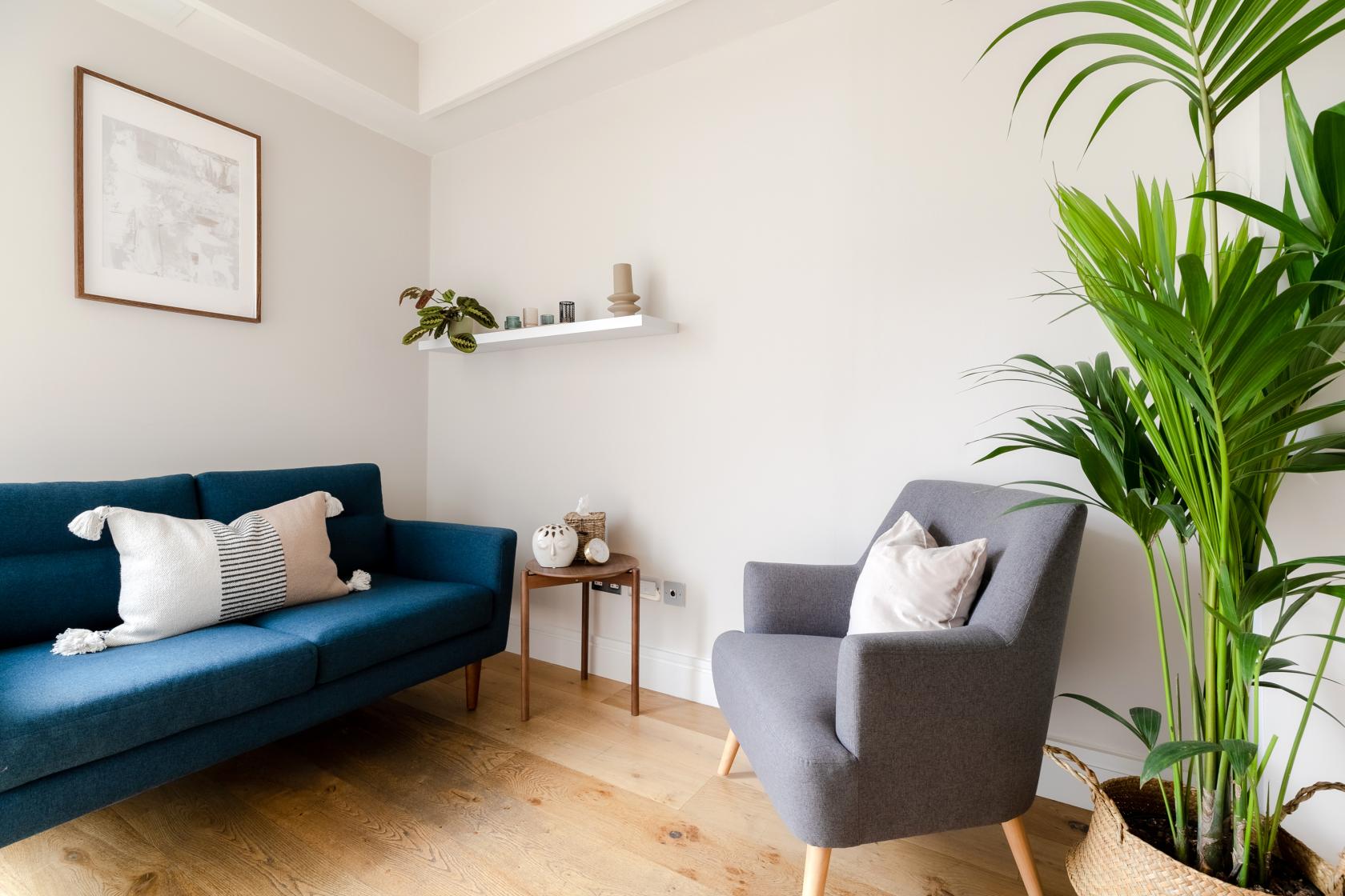 A meeting centre lounge with a blue sofa, grey armchair, potted plant, and wall art at CuraRooms Marylebone.