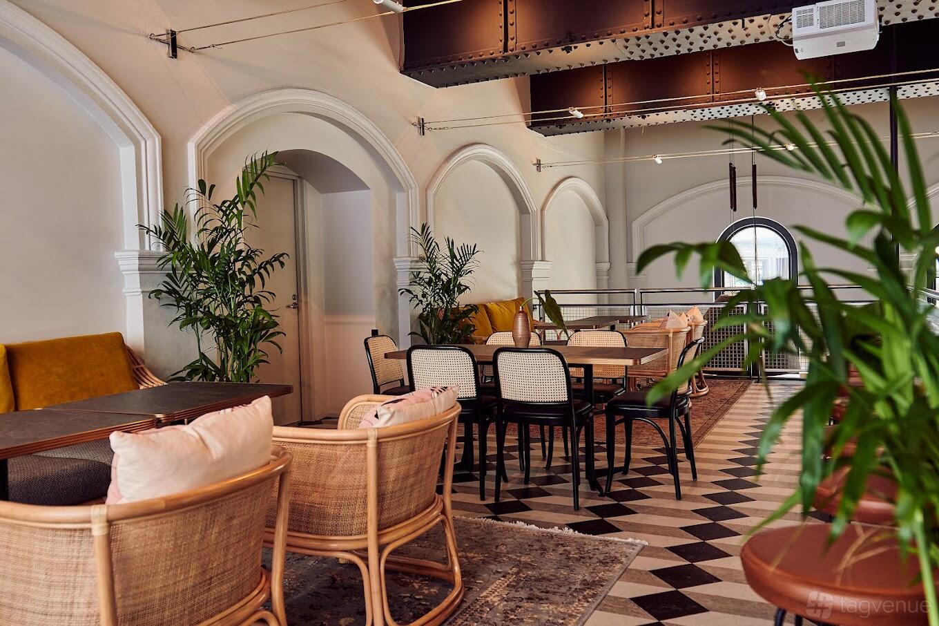 An upstairs event space in a pub with checkered floors, rattan chairs, arched doorways, and indoor plants at Pumphouse Sydney.