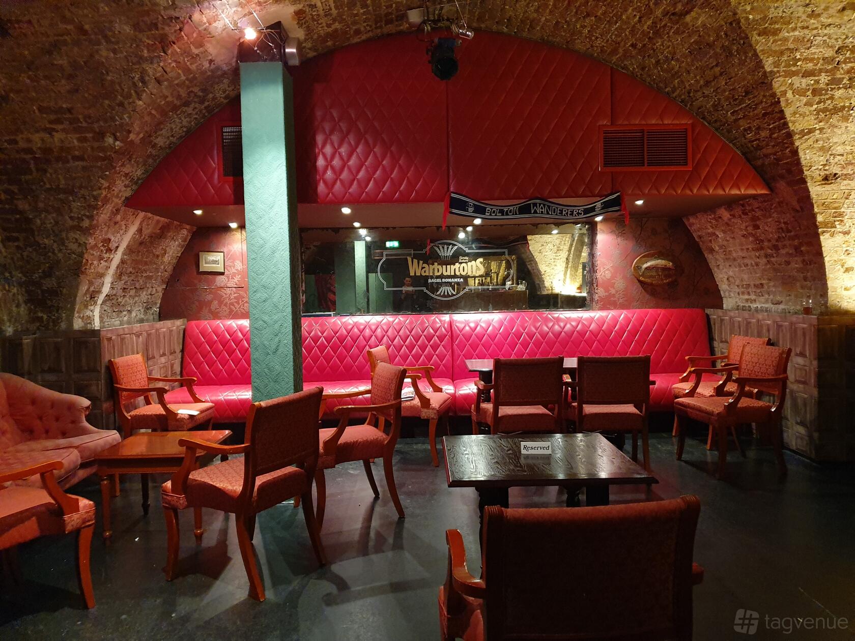 An event venue with arched exposed brick ceilings, red tufted banquette seating, and vintage armchairs at Adam House Event Space.
