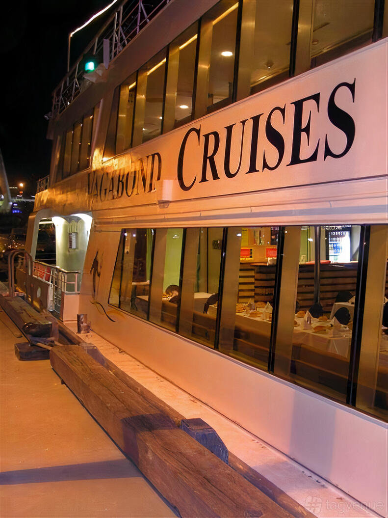 A docked cruise boat with large windows revealing set dining tables and warm interior lighting at M.V. Vagabond Spirit.