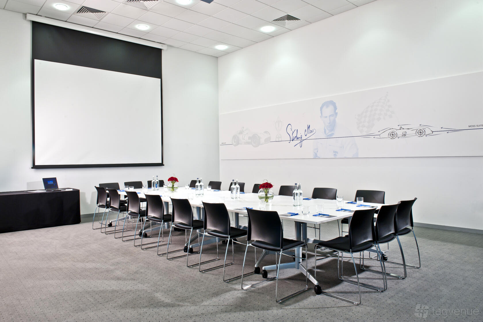 A meeting room with a long conference table, black chairs, wall art, and a ceiling-mounted projector at Mercedes-Benz World.