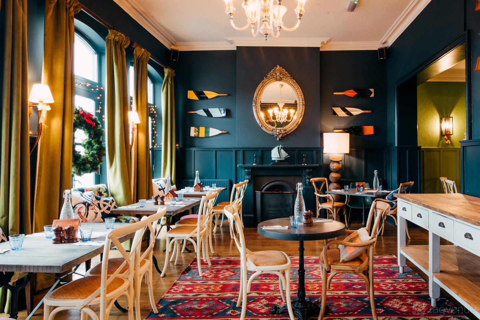 An event space in a pub with arched windows, wooden chairs, colorful rugs, and decorative oars at The Blue Anchor.