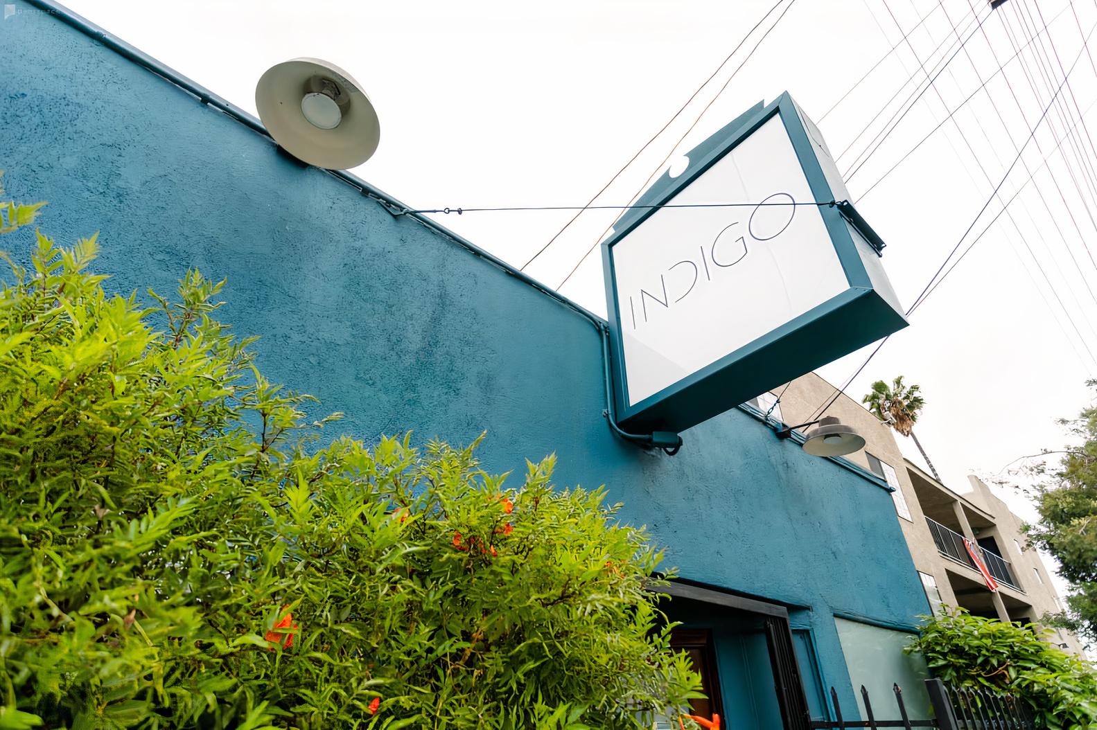 A film and photo studio with a blue exterior wall, large hanging sign, and greenery at Indigo Studio LA