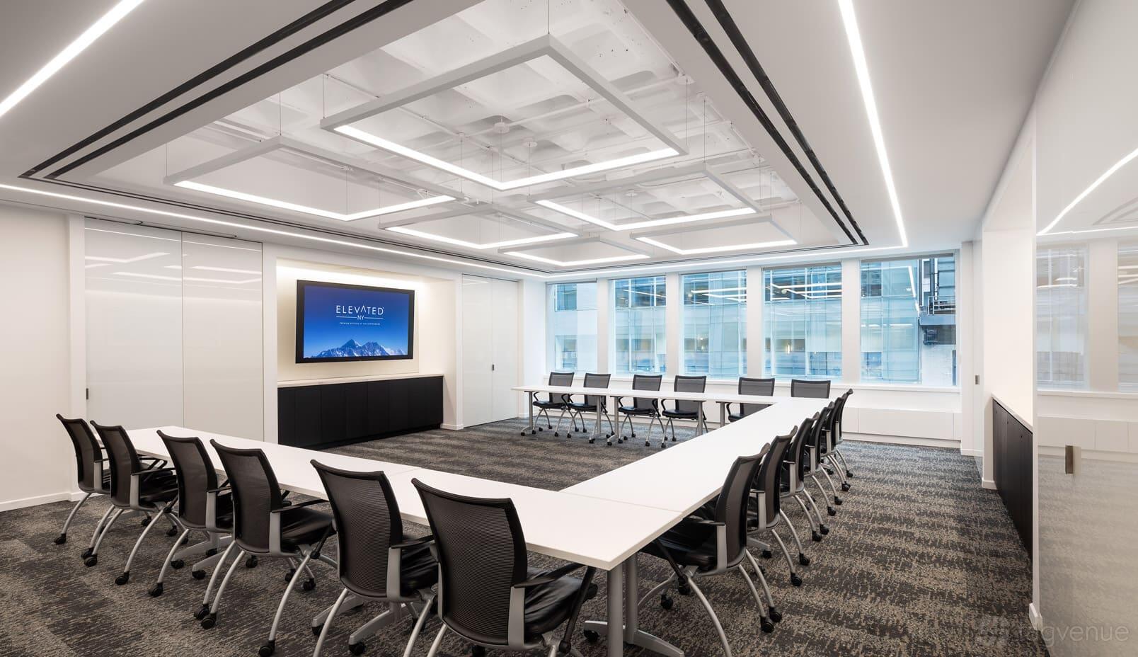 A meeting room with U-shaped tables, ergonomic chairs, floor-to-ceiling windows, and a wall-mounted presentation screen at ElevatedNY.