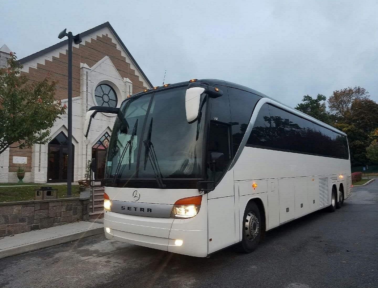 A large white party bus parked outside a church with stone steps and arched windows at Famous Drive.