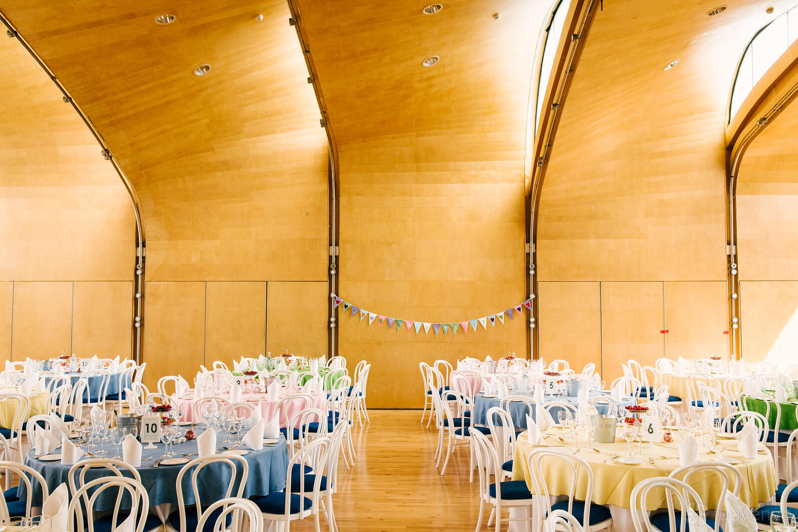 An art studio with high, curved wooden ceilings, pastel round tables, and bunting at Siobhan Davies Dance Studios.