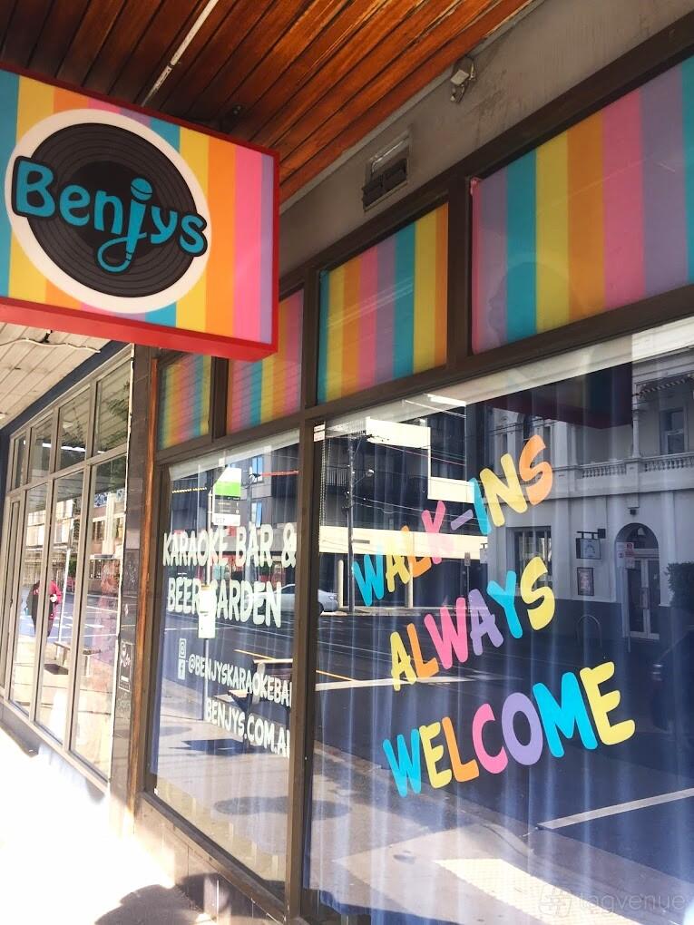 A pub with colorful striped window decals and painted signage at Benjys Karaoke Bar.