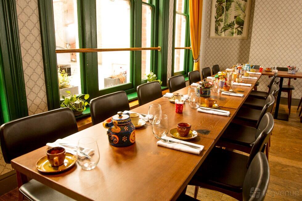 A dining room with a long wooden table set with teapots, cups, and natural light from large windows at Cinnamon Bazaar.