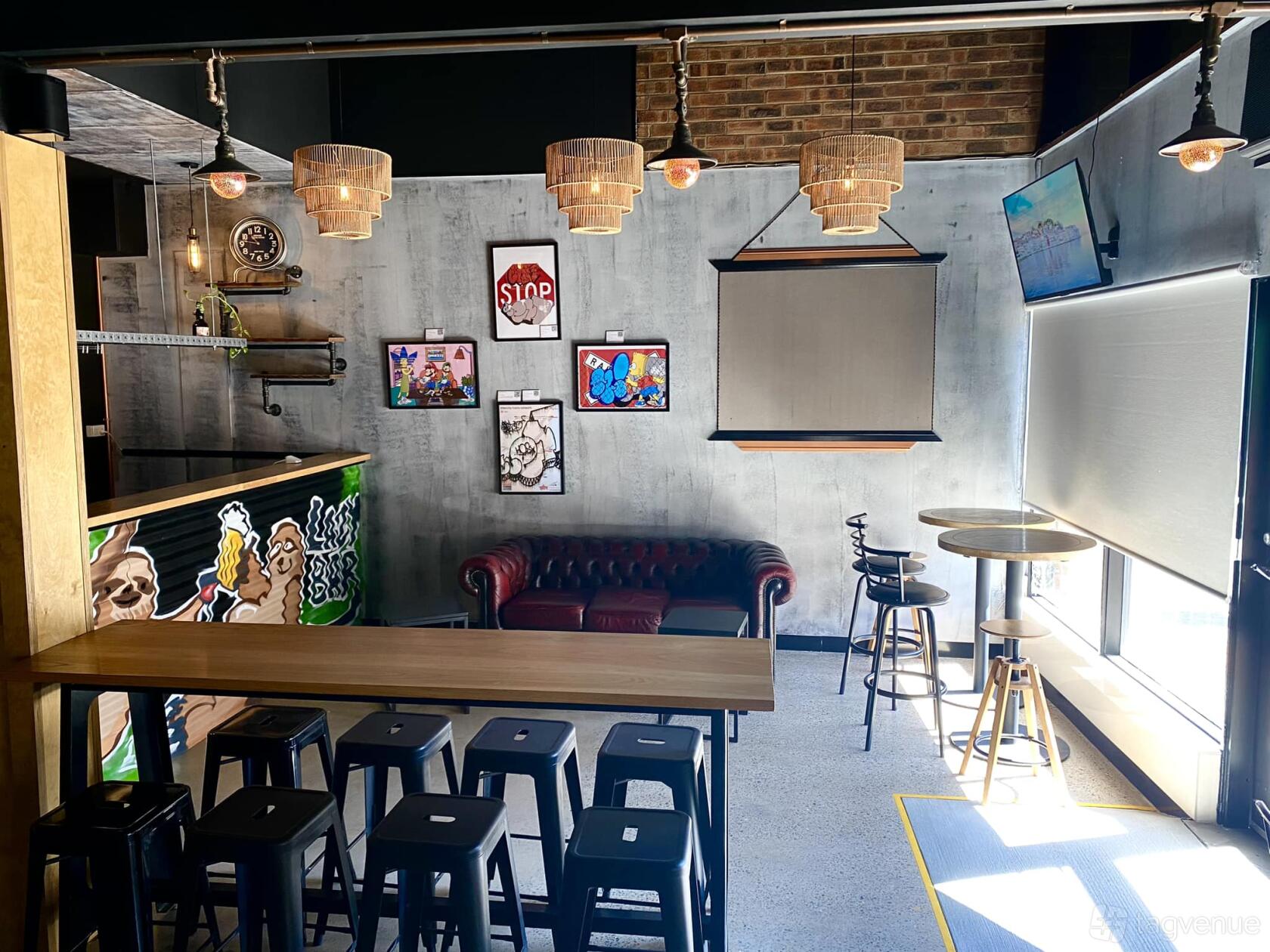An event space in a bar with industrial gray walls, exposed brick, pendant lights, and eclectic wall art at Lazy Bar Hurlstone Park.