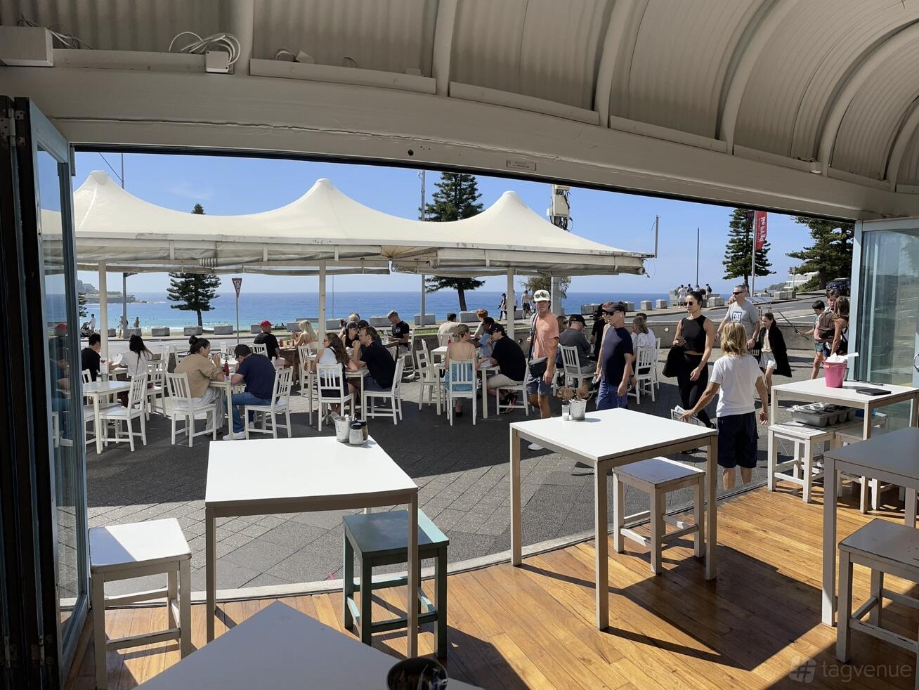 A beachfront cafe with open-air seating, white tables and chairs, and ocean views at Lamrock Cafe Bondi Beach.