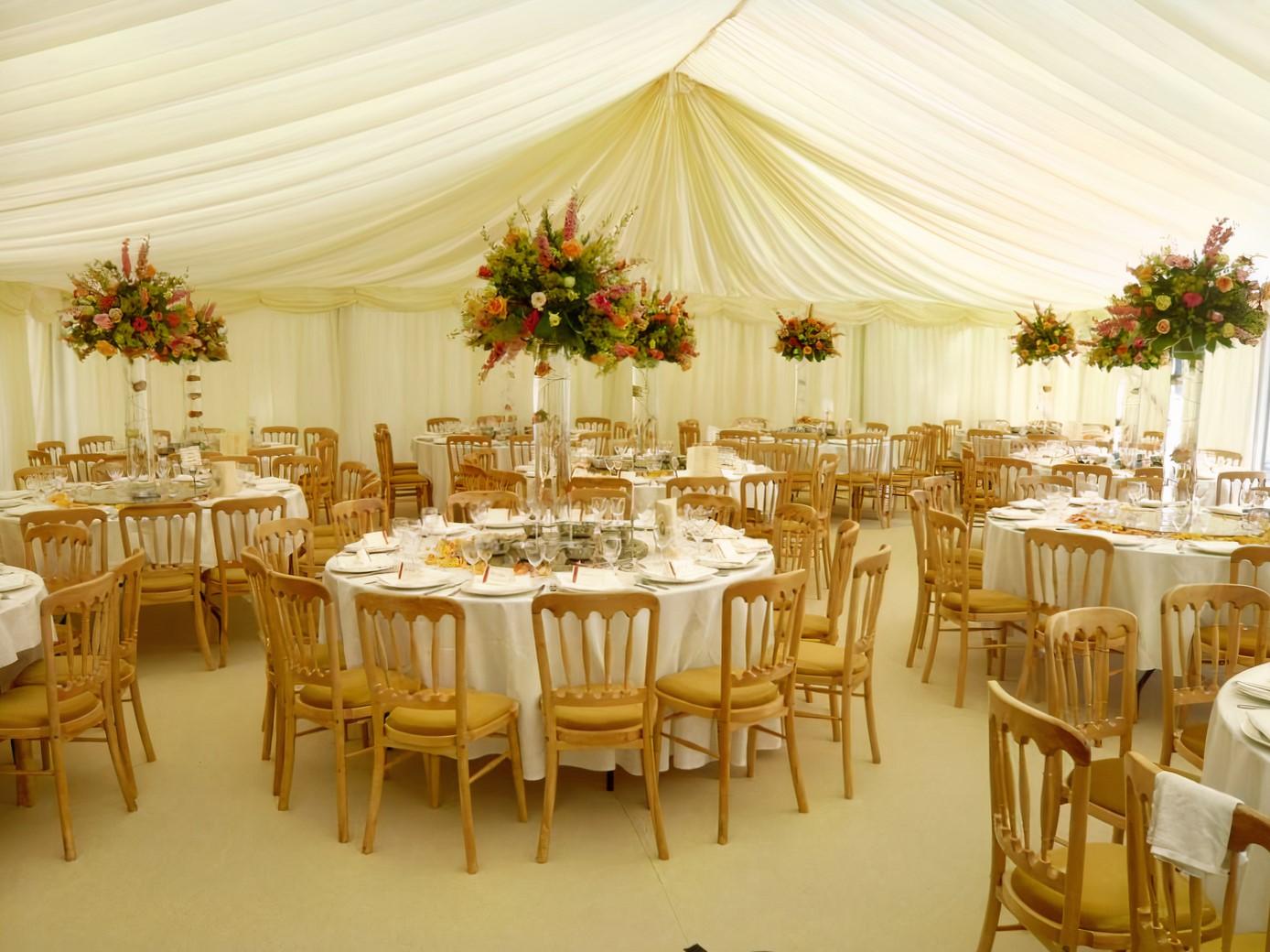 A terrace event space with draped white canopy, round tables set with white linens, and tall floral centerpieces at Vauxhall Arches.