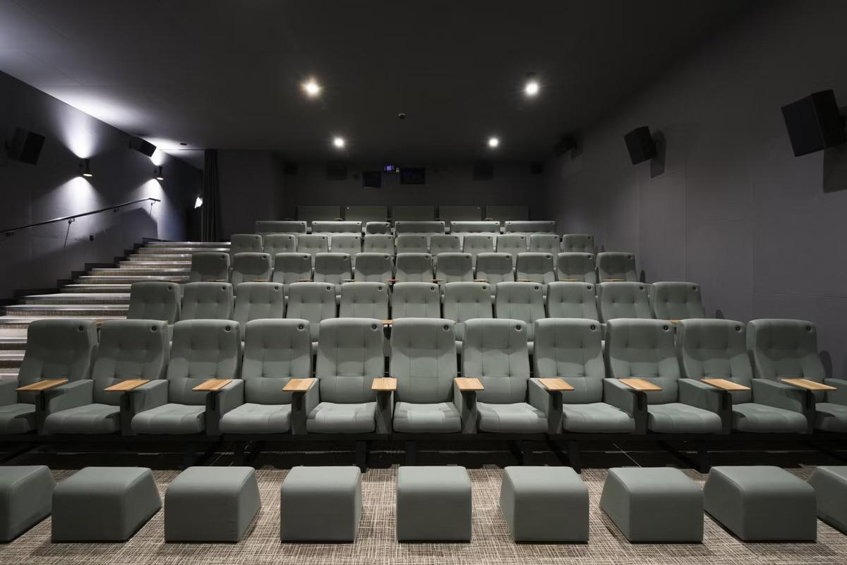 A cinema screening room with tiered rows of plush gray seats, arm rests, and footstools at Curzon Aldgate.