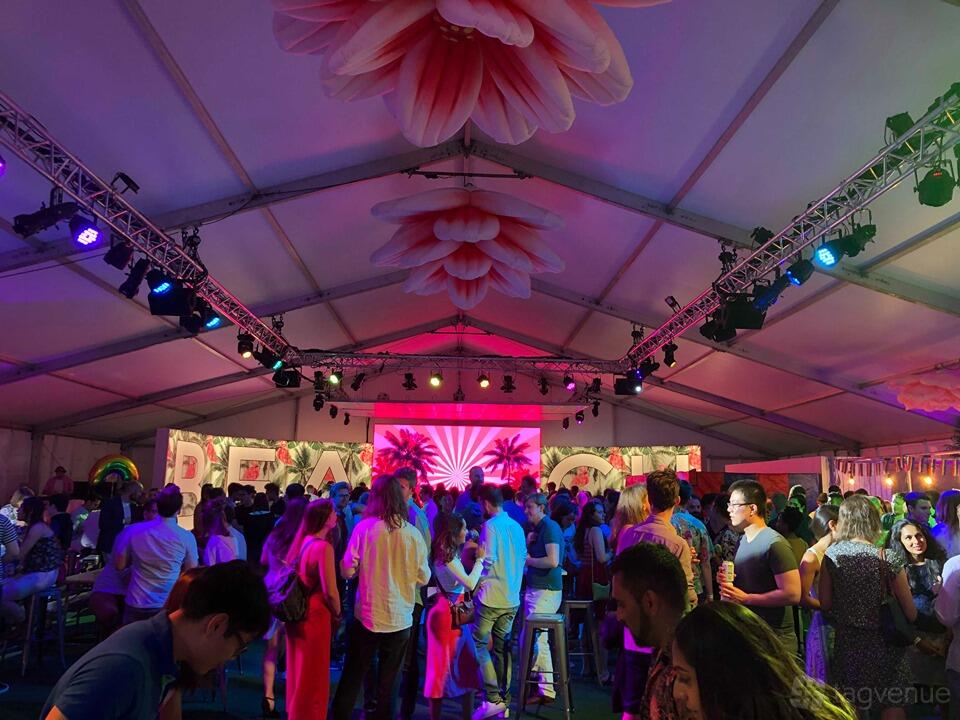 An event venue with a large tented space, colorful lighting, and a crowd gathered beneath floral ceiling decor at The London City Beach.