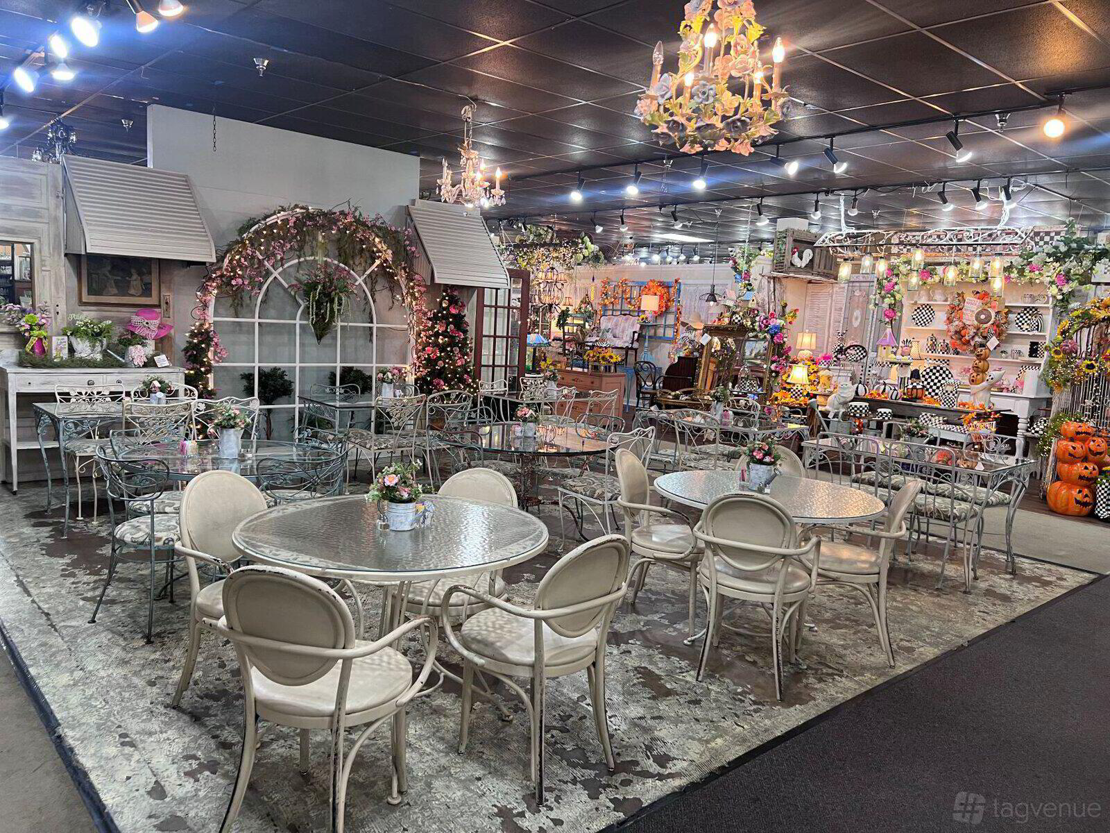 A cafe with round glass tables, white chairs, chandeliers, and floral decor at Chocolate Angel Cafe & Tea Room - High Street.