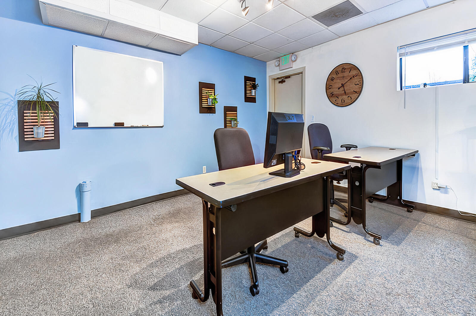 A coworking space with two desks, office chairs, a wall-mounted whiteboard, and a clock at West Seattle Coworking-Junction.