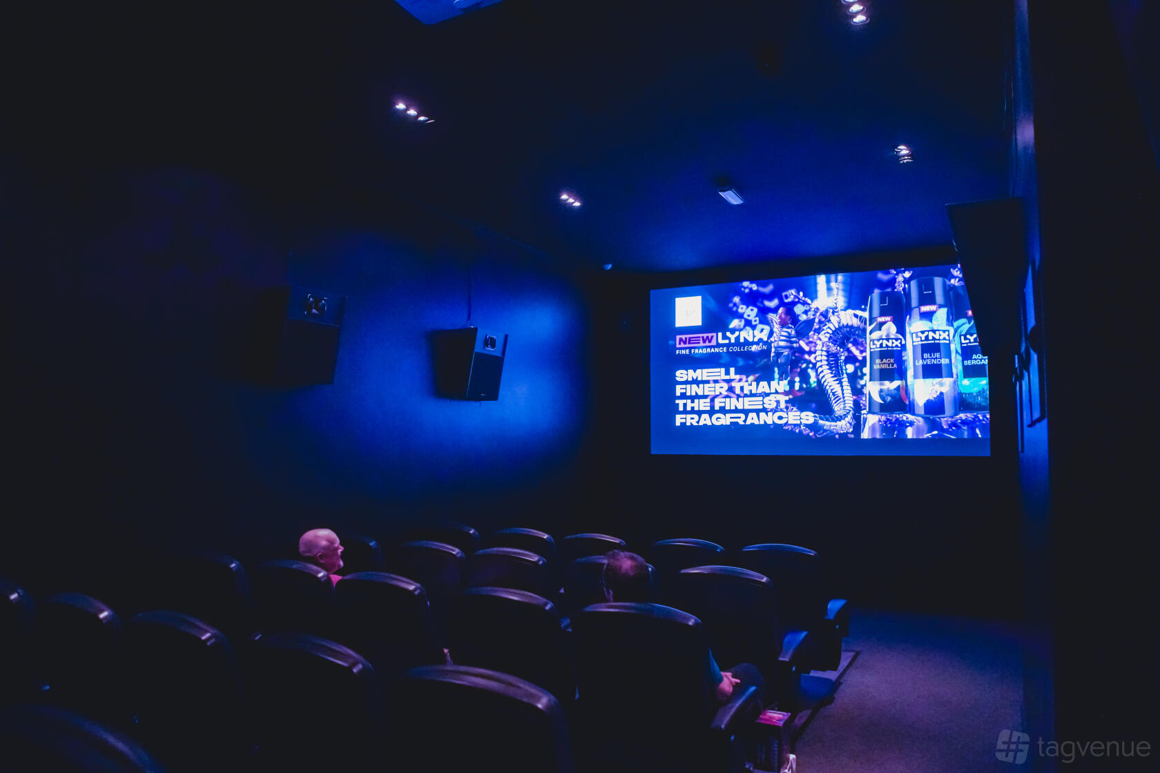 A cinema screening room with black theater seats, wall-mounted speakers, and a large projection screen at Mockingbird Cinema & The Nest Bar and Kitchen.