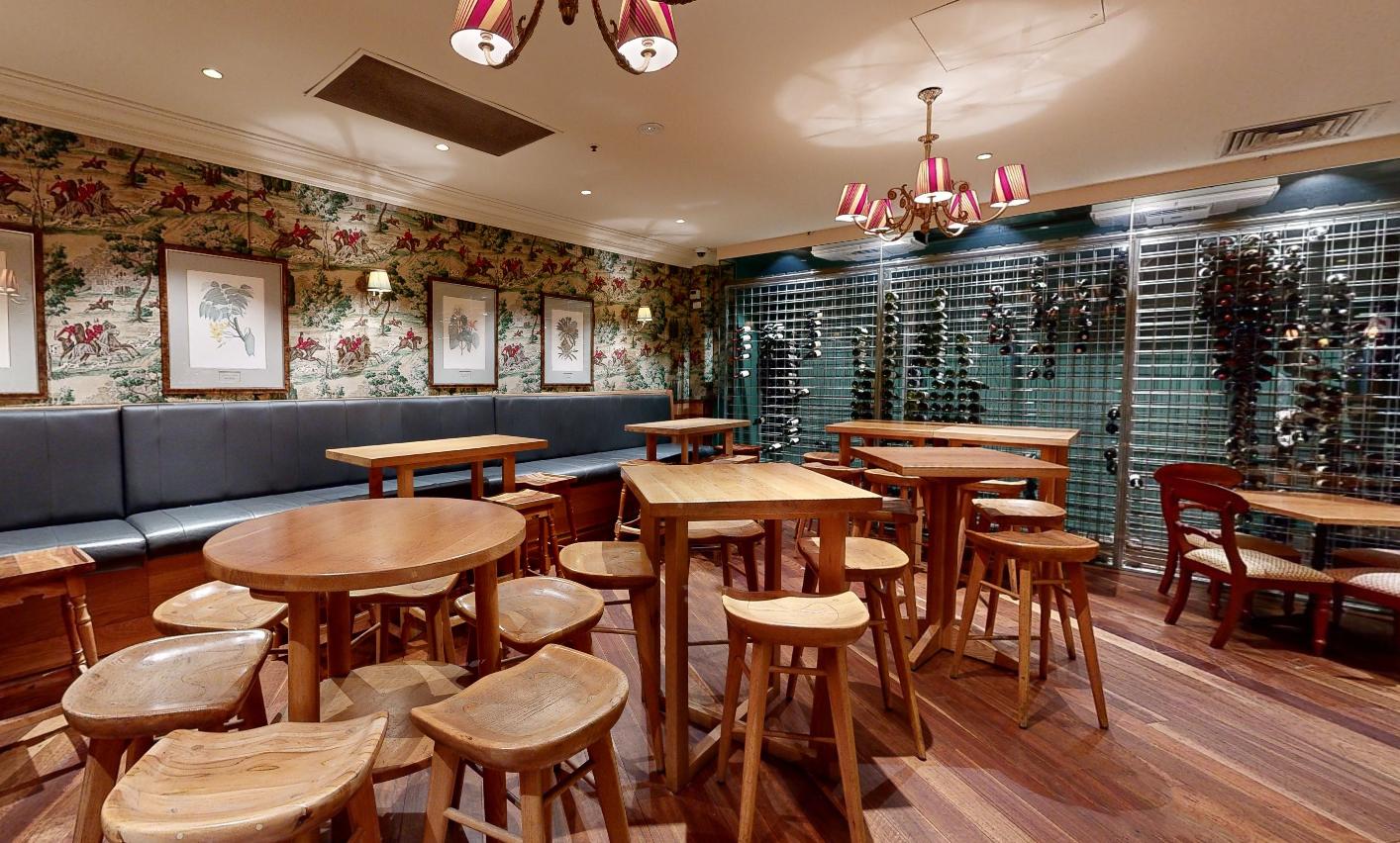 An event space with wooden tables, round stools, floral wallpaper, and a glass wine display at Pig ‘N’ Whistle - Indooroopilly.