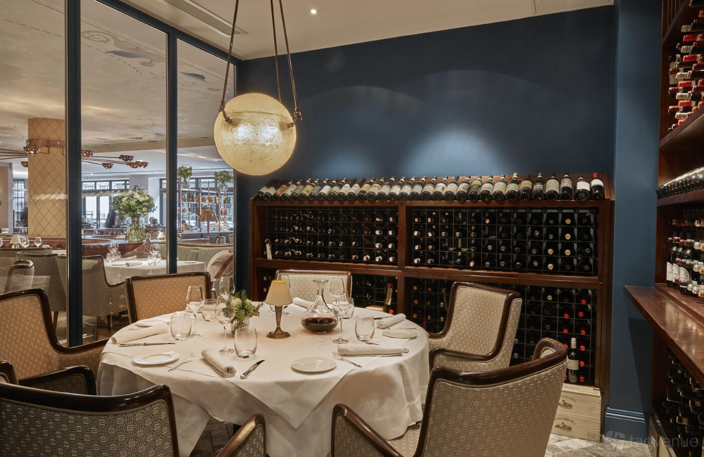 A dining room with a round table set with white linens and a wall of wine racks at Sartoria.