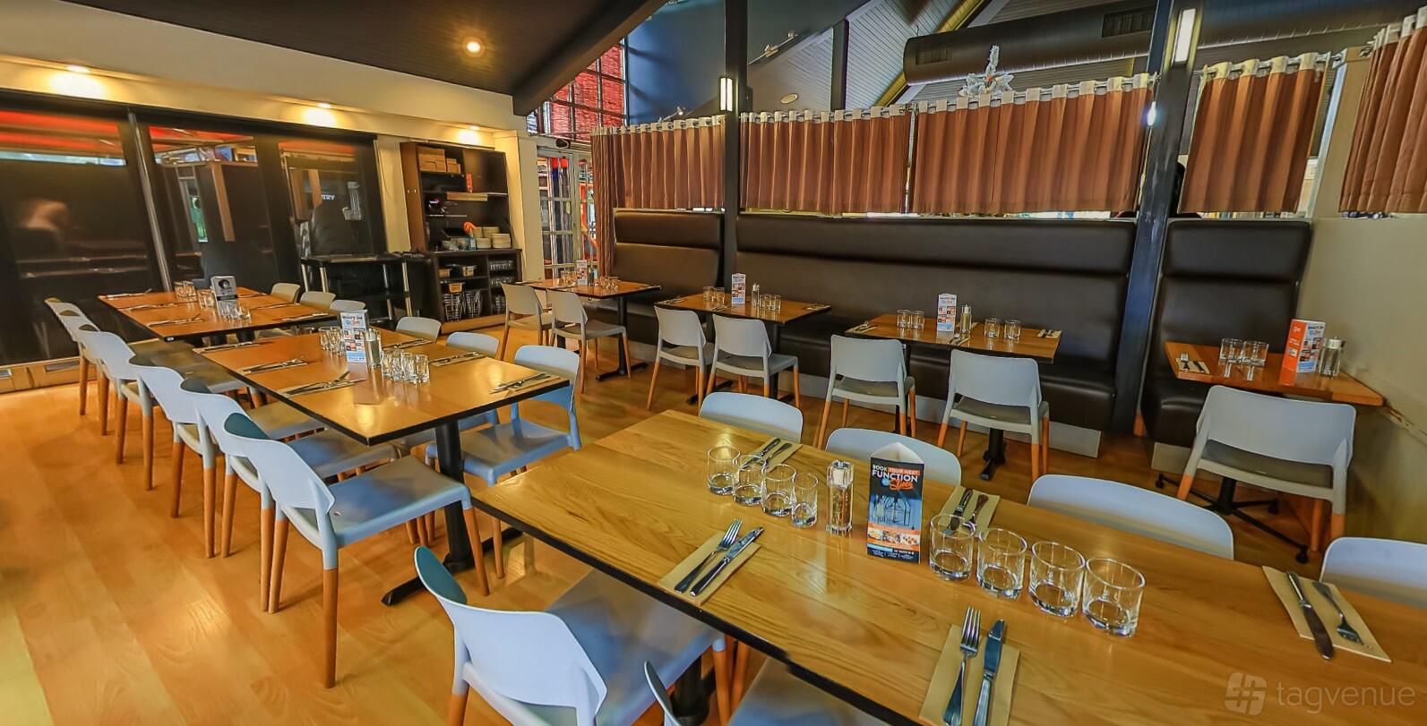 A dining room with wooden tables, white chairs, glassware, and a long upholstered banquette at Slices Keilor.