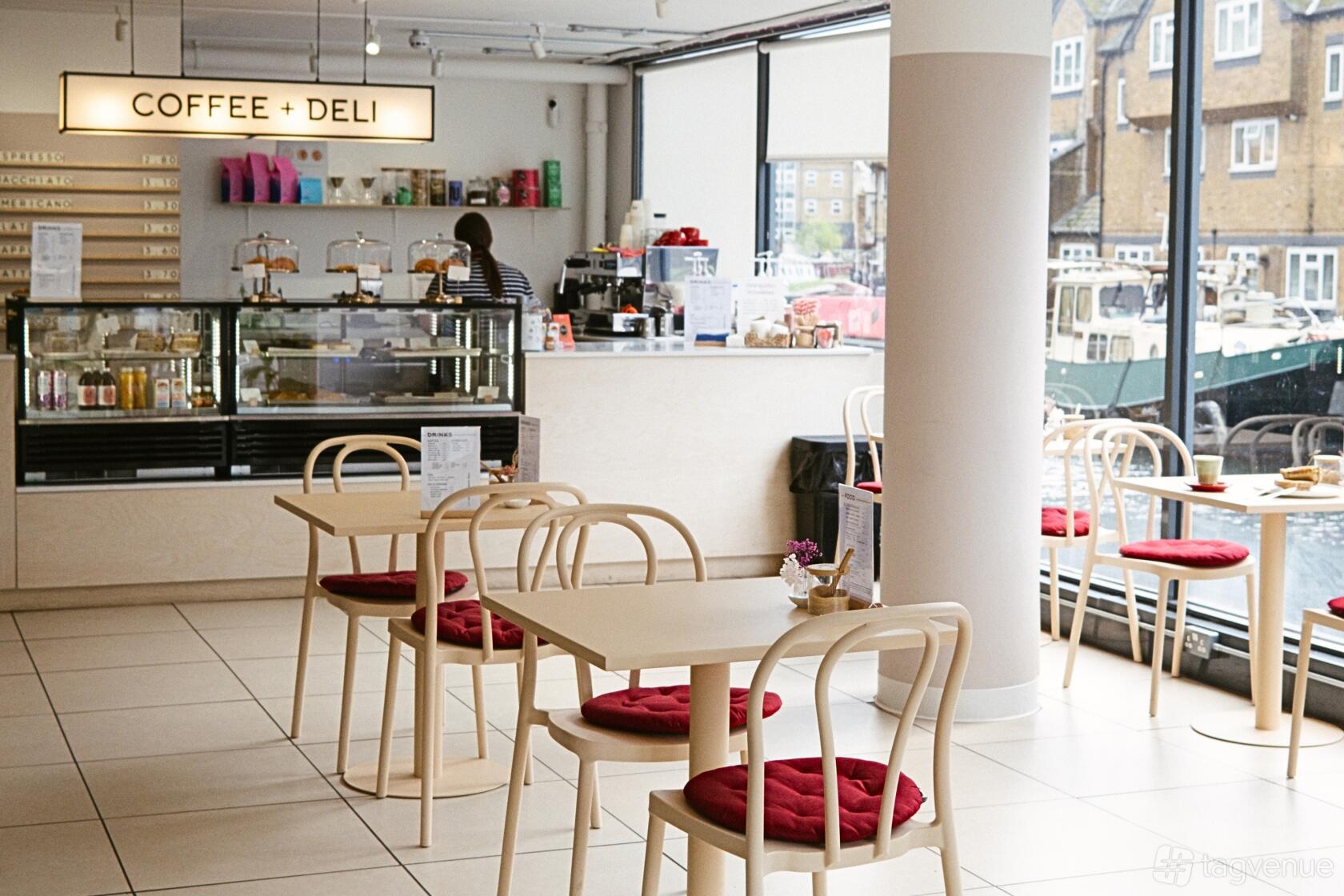 A cafe with floor-to-ceiling windows, light wooden tables, red seat cushions, and a pastry counter at W10 Coffee + Deli.