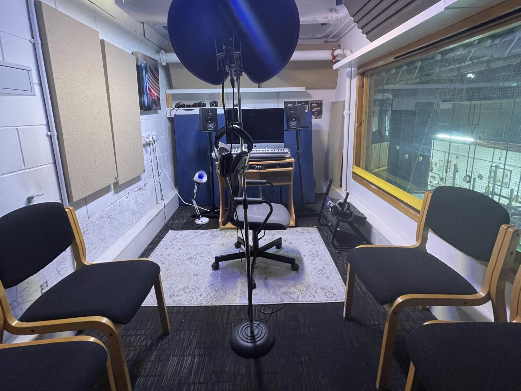 A recording studio with soundproof panels, a central microphone, studio monitors, and chairs at The RecordShop.
