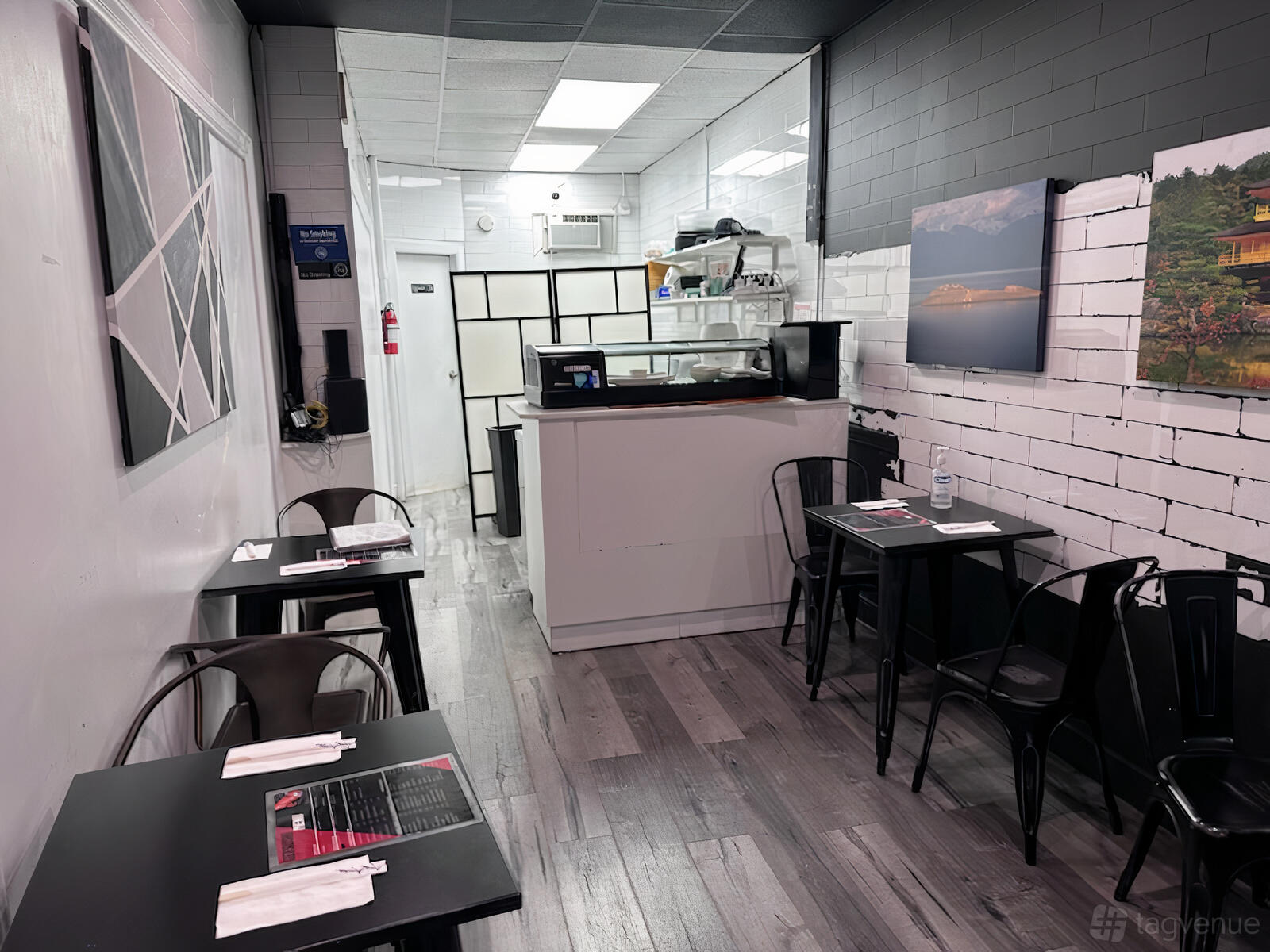 A restaurant with black tables, metal chairs, and framed artwork on white brick walls at Ger Sushi.