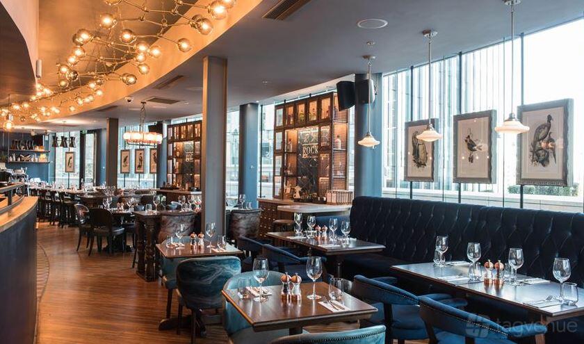 A restaurant with tufted banquette seating, wood tables set with glassware, and large windows at Rocket.