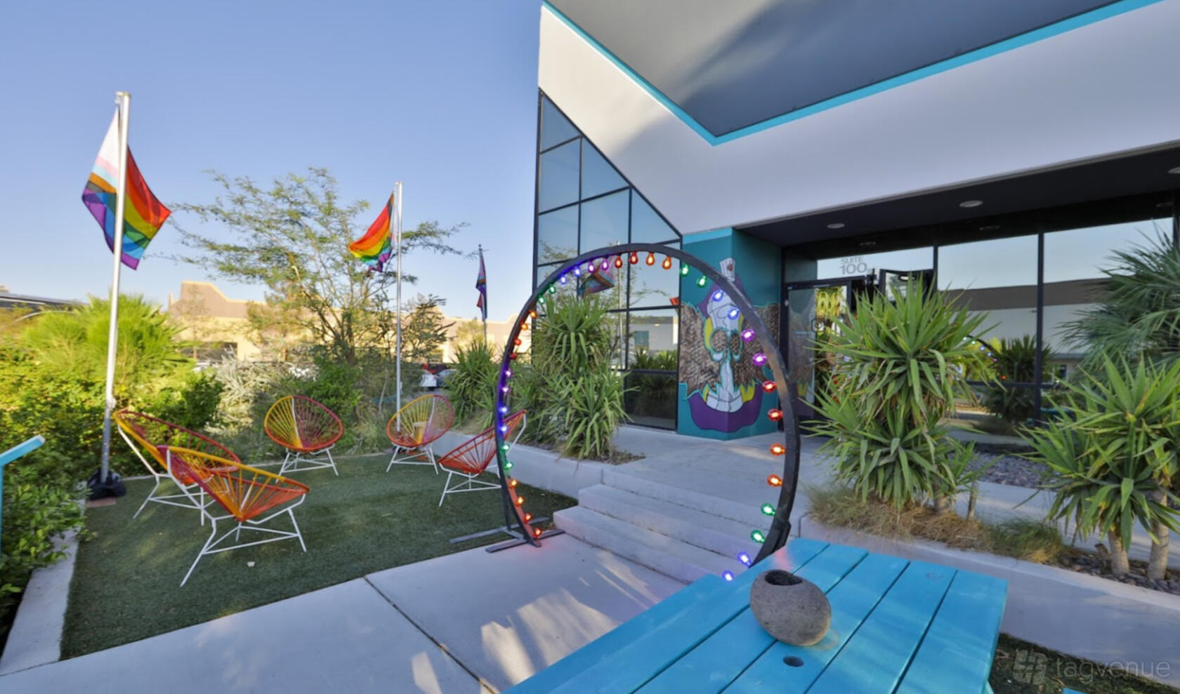 A warehouse entrance with a colorful light arch, patio seating, and pride flags at StarBase Las Vegas.