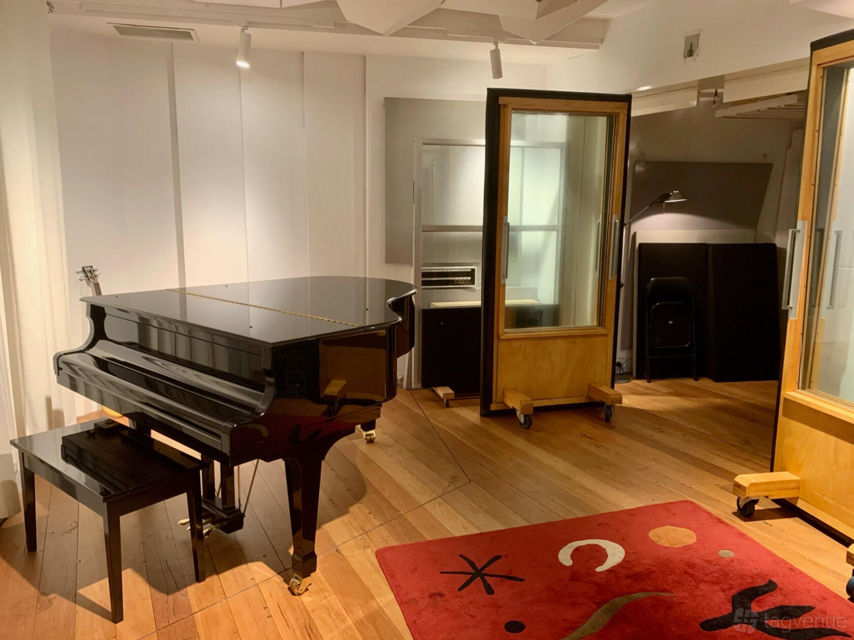 A recording studio with a black grand piano, wood floors, and portable acoustic panels at Electric Avenue Studio.