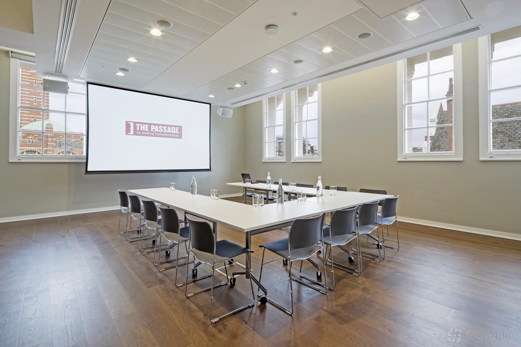 An event venue with large windows, wood floors, and a U-shaped table setup with water bottles at Cathedral View.